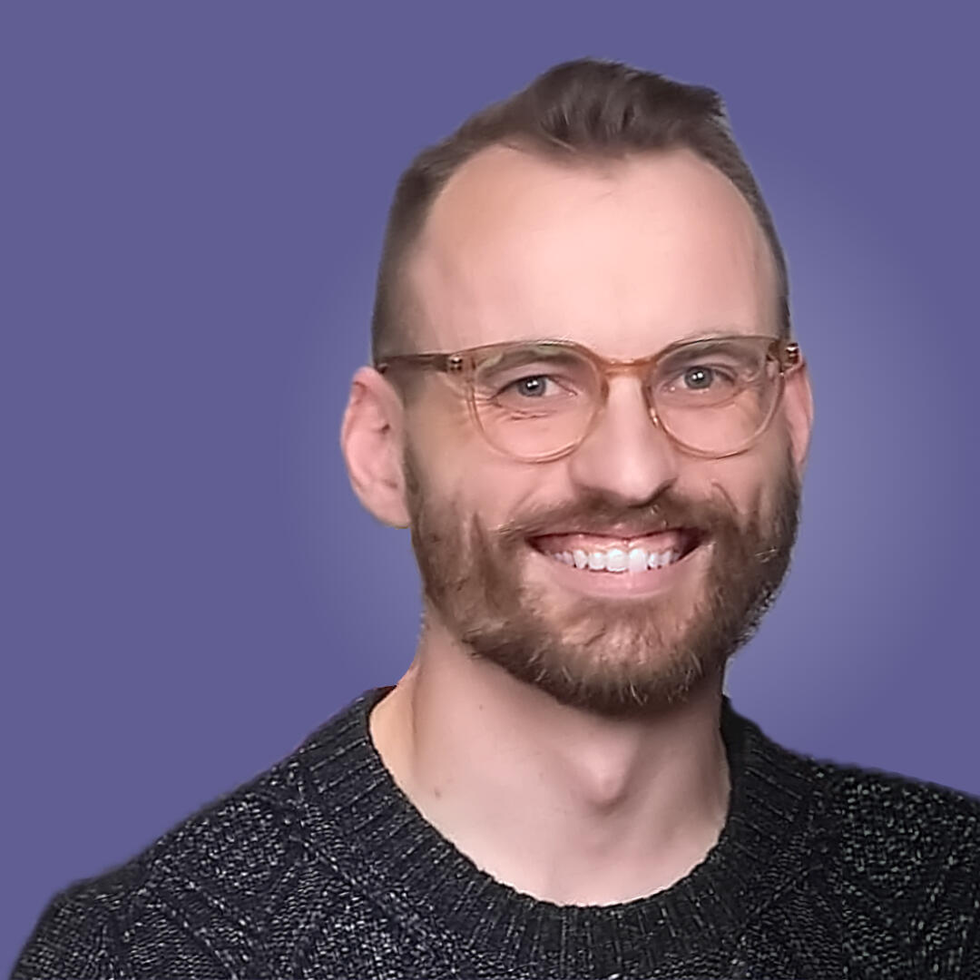 Photo of Derek Moeller-Smith from the shoulders up. He is a white man with light brown hair, glasses, and a short beard. He is smiling and wearing a black knit sweater.